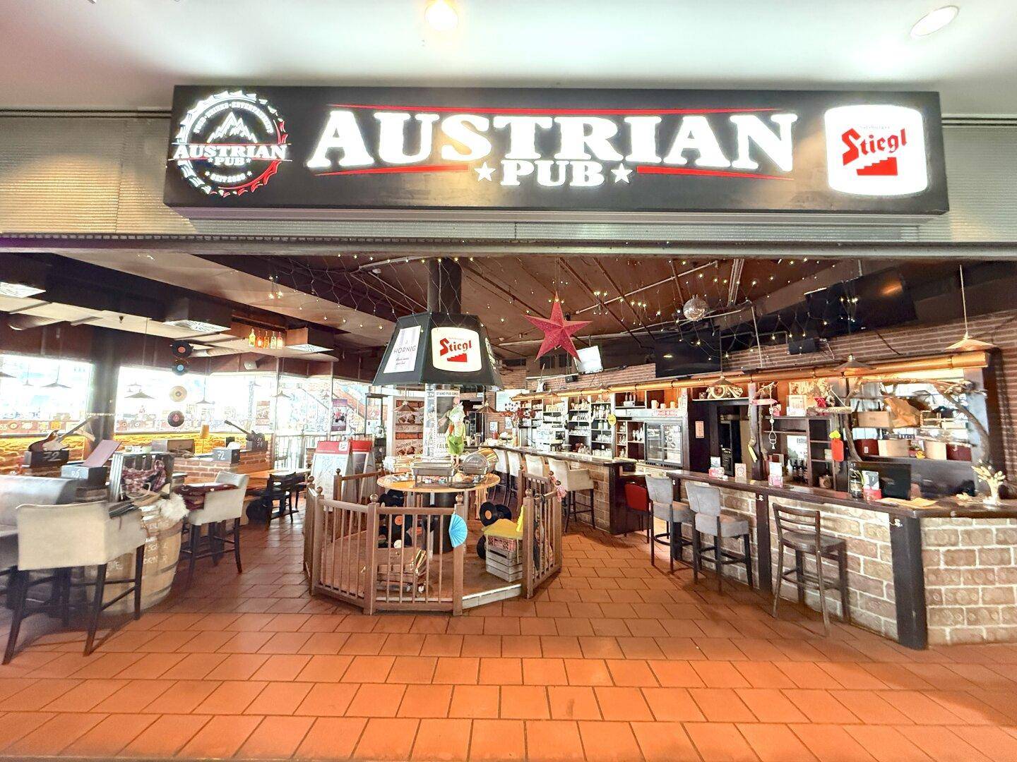 Eingangsbereich des Austrian Pubs mit Blick auf den Gastraum und die Bar, gekennzeichnet durch das große Leuchtschild.