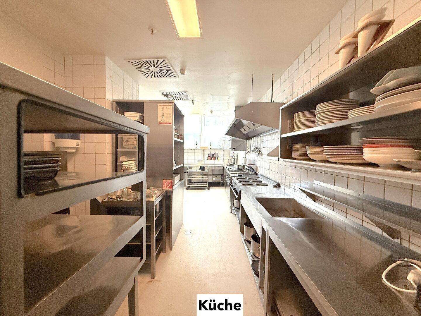 Lange Reihe von Edelstahl-Arbeitsflächen und Regalen in einer professionellen Küche, bereit für den Betrieb.