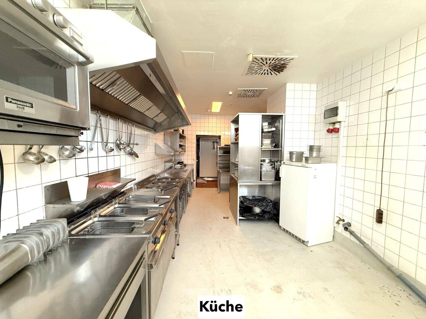Geräumige Großküche mit umfangreicher Ausstattung aus Edelstahl, inklusive Mikrowelle und Kühlschrank.