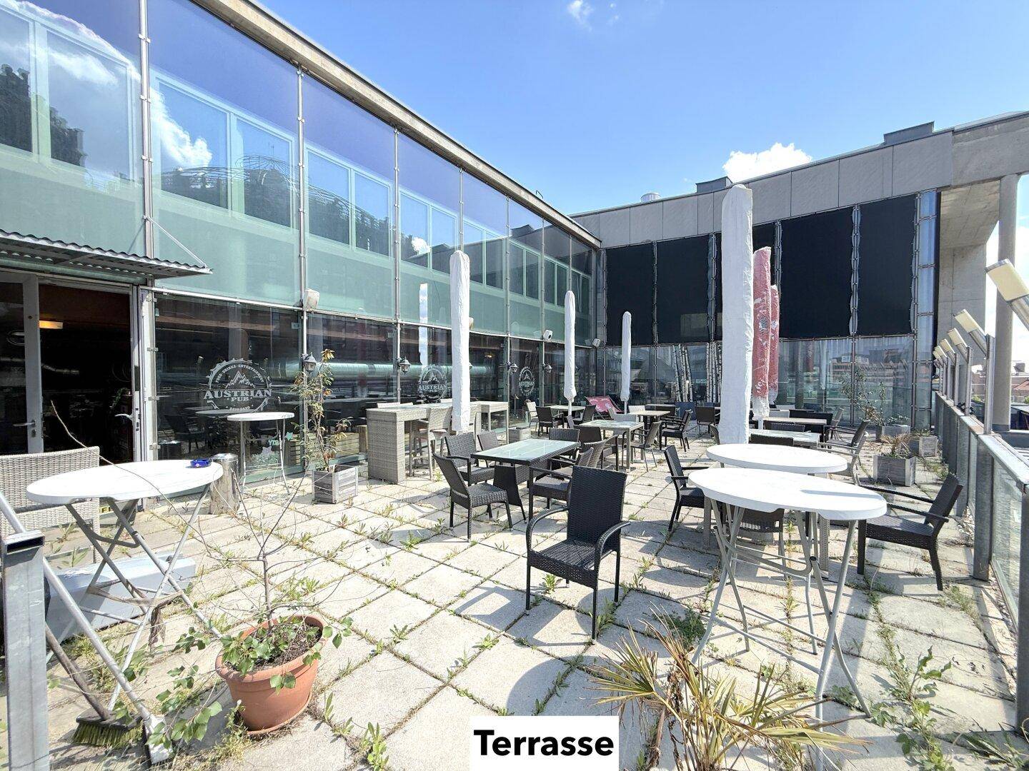 Weitläufige Terrasse mit verschiedenen Sitzgruppen und Blick auf die moderne Glasfassade des Gebäudes.