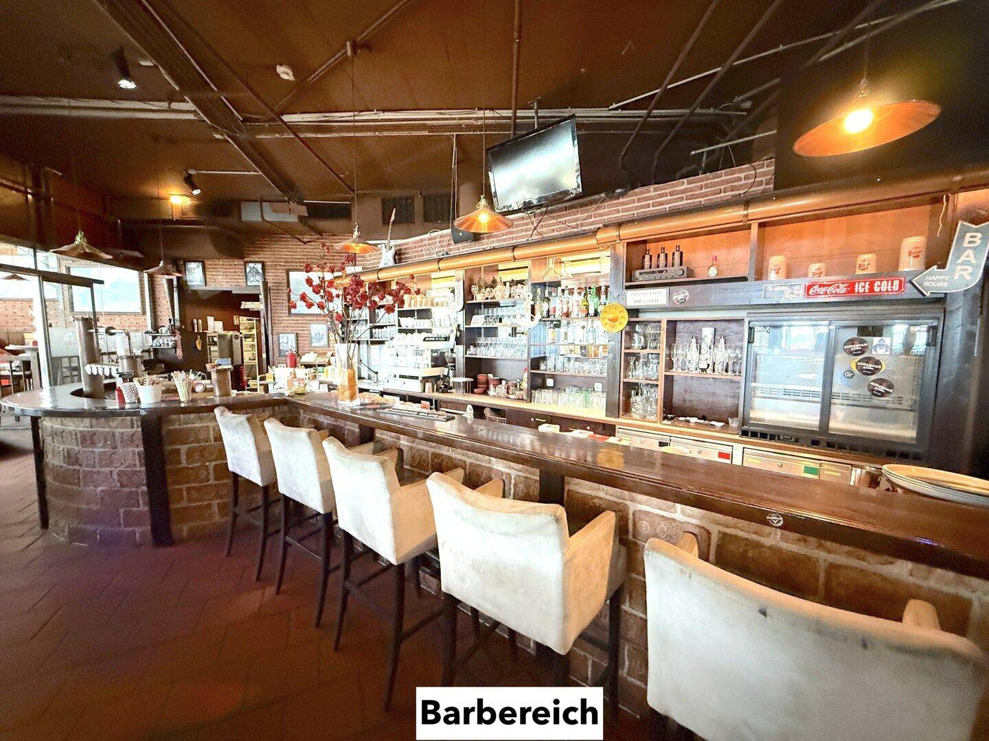 Bar-Bereich mit bequemen Barhockern, einer langen Theke und Regalen voller Gläser und Flaschen.