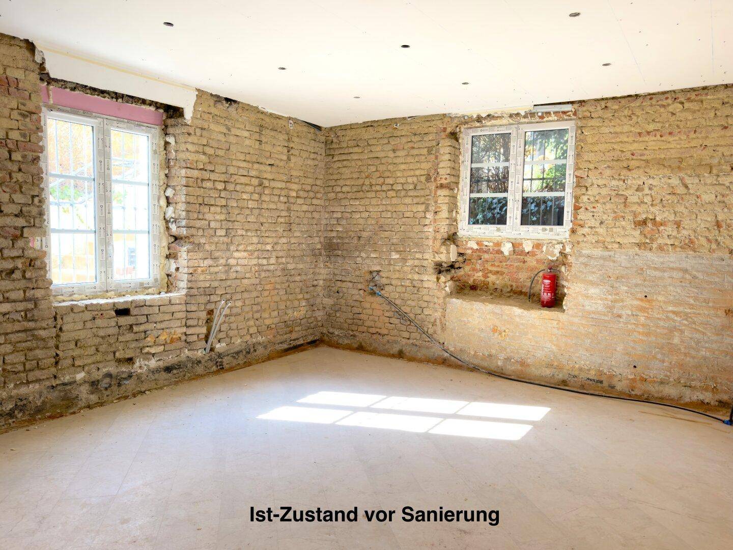 Raum im Ist-Zustand vor der Sanierung mit freigelegten Ziegelwänden und Fenstern.