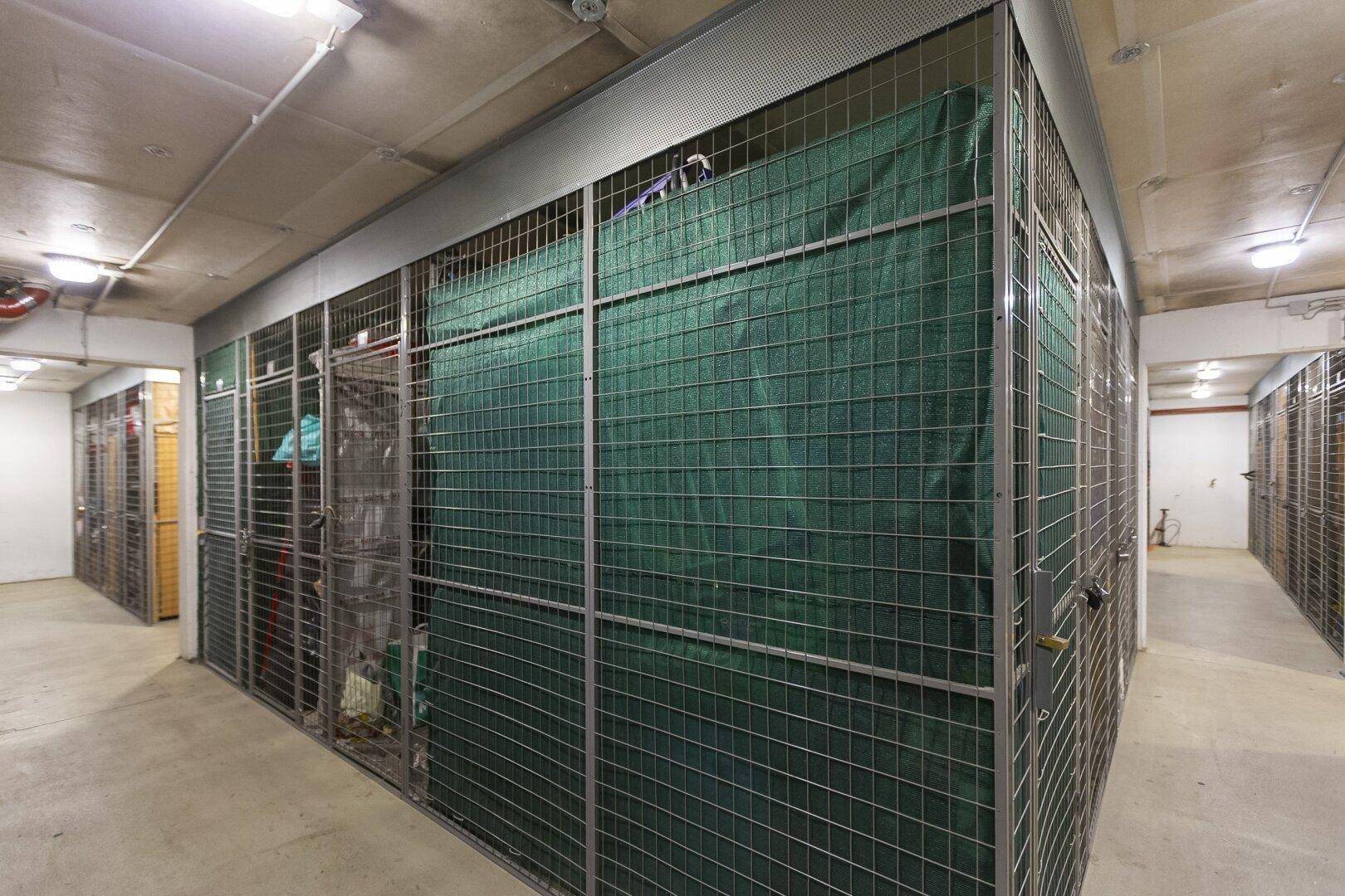 Kellerabteile mit Gitterwänden und grünen Planen für zusätzlichen Stauraum.