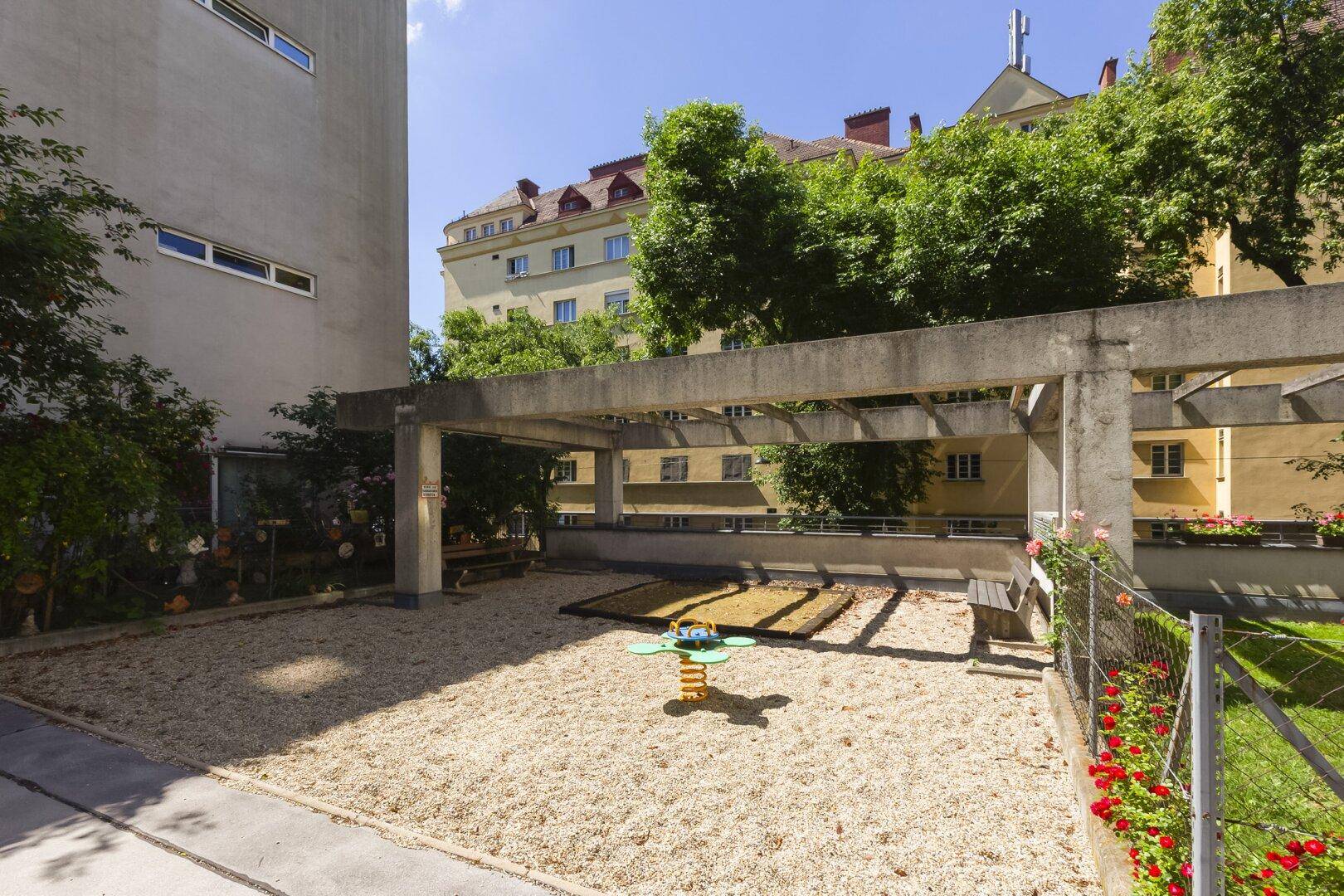 Kinderspielplatz mit Sandfläche und Spielgeräten in einem begrünten Innenhof.