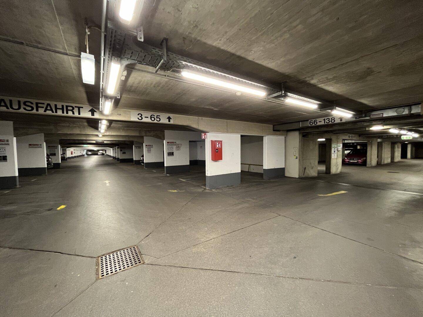 Weitläufige Tiefgarage mit zahlreichen Stellplätzen, Betonstruktur und Notausgangsbeschilderung.