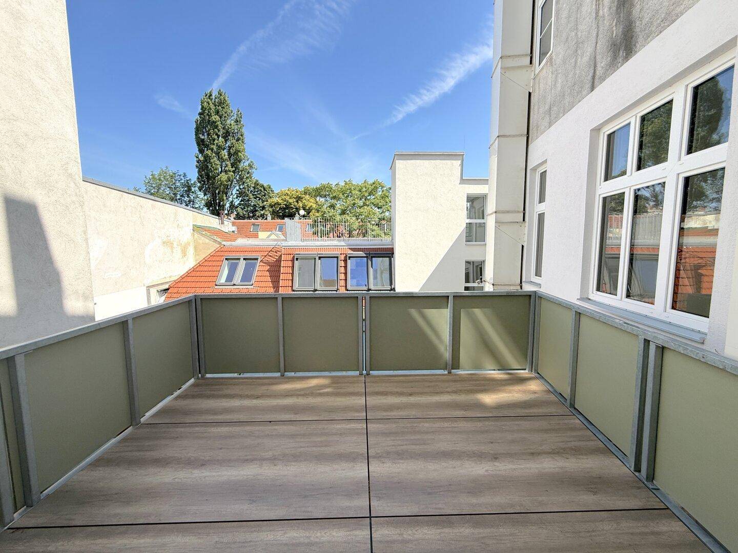Moderner Balkon mit Fliesenboden und Blick auf umliegende Gebäude und Bäume unter blauem Himmel.
