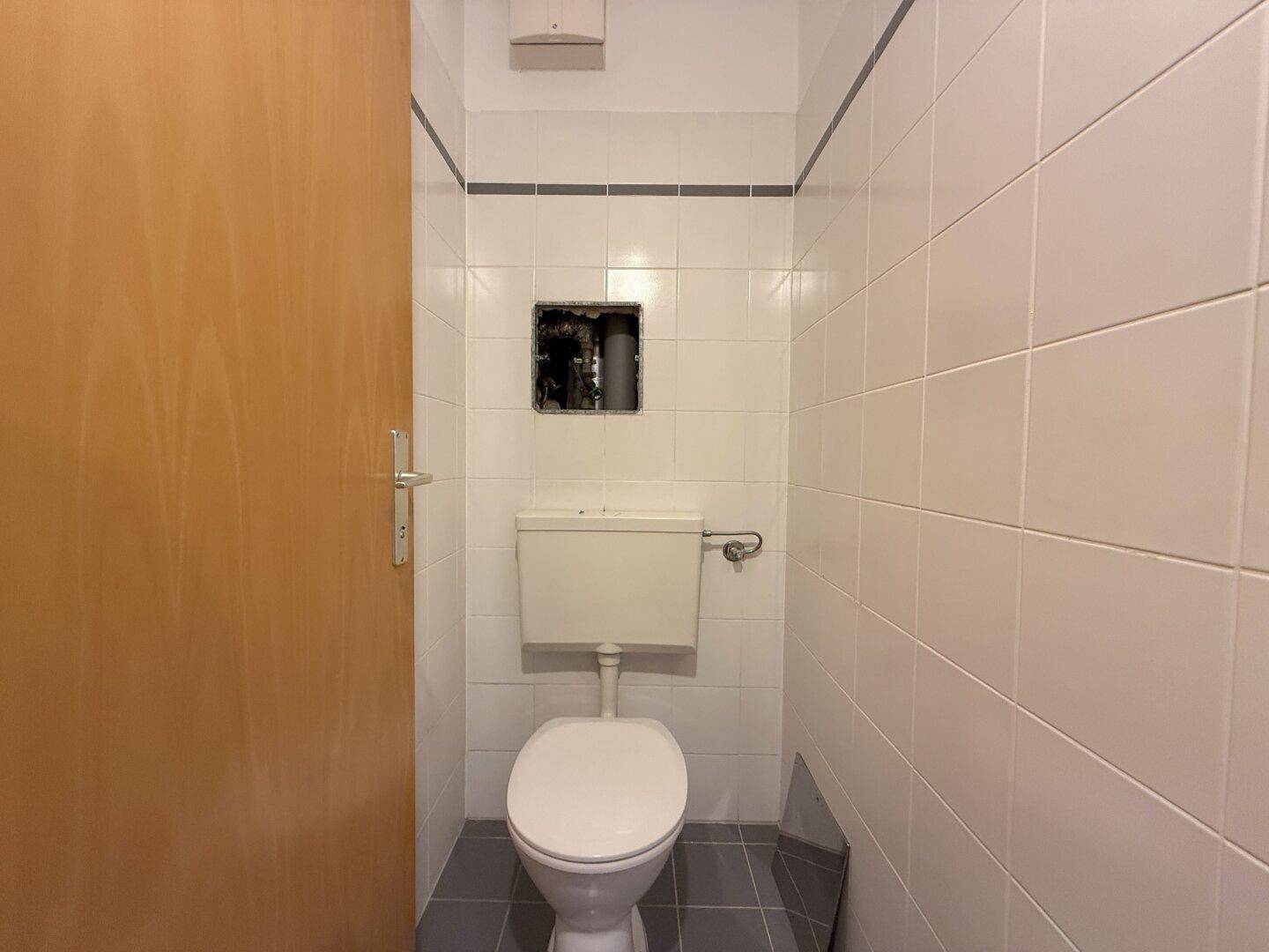 Separate Toilette mit weiß gefliesten Wänden und einem einfachen WC.