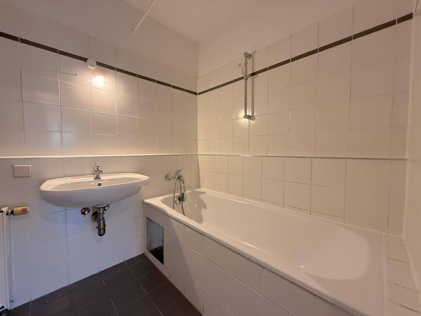 Badezimmer mit weiß gefliesten Wänden, einer Badewanne und einem Waschbecken.