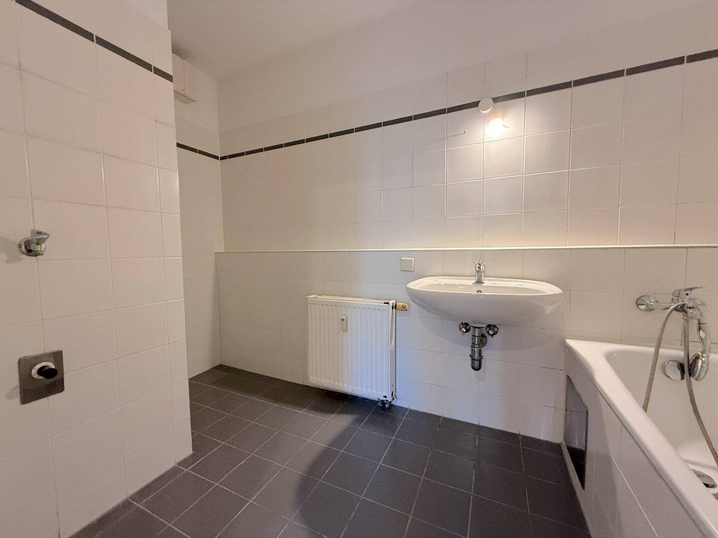 Badezimmer mit weißen Wandfliesen, einem Waschbecken und einer Badewanne.