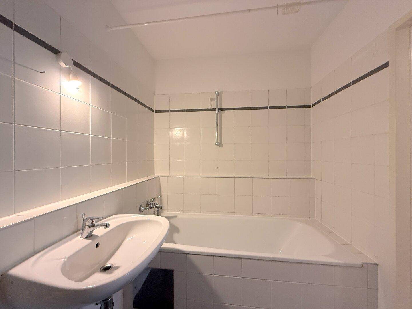 Badezimmer mit weiß gefliesten Wänden, einer Badewanne und einem Waschbecken.