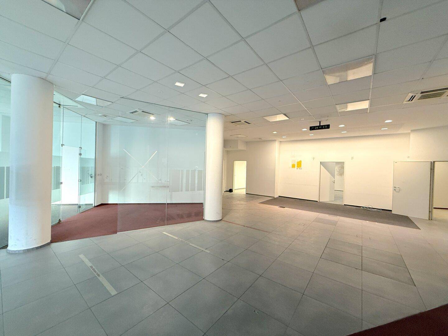 Weitläufiger Gewerberaum mit Glaswänden, Fliesenboden und einer Treppe hinter der Glasabtrennung.