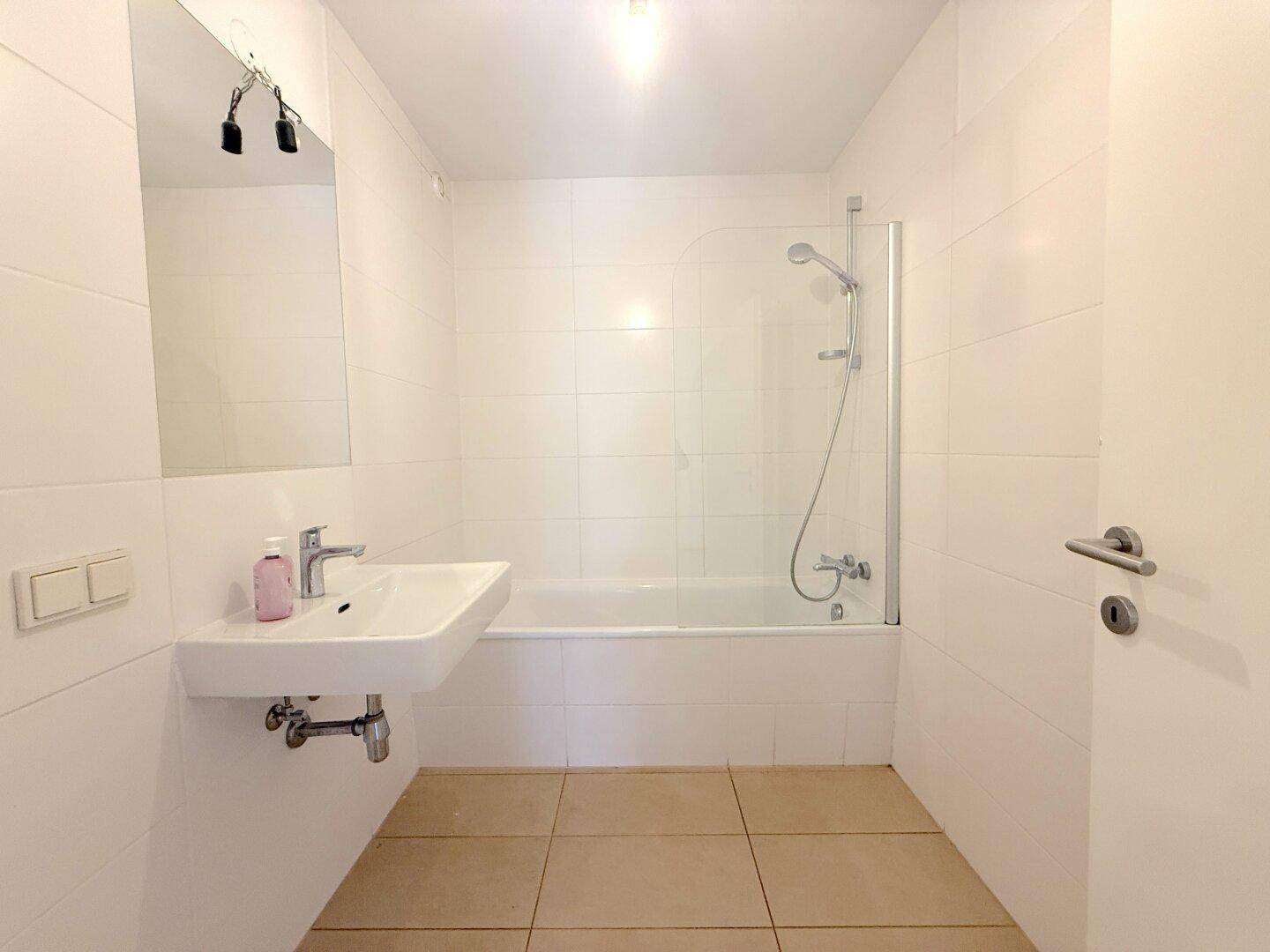 Modernes Badezimmer mit weißen Fliesen, Waschbecken und Badewanne mit Duschabtrennung.