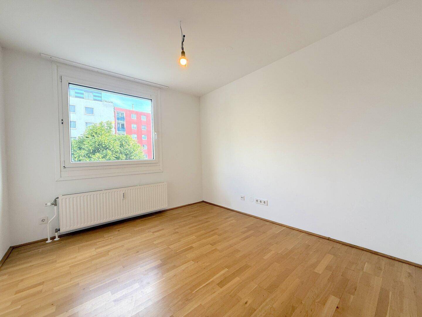 Helles Schlafzimmer mit Parkettboden und einem großen Fenster, das den Raum mit Licht füllt.