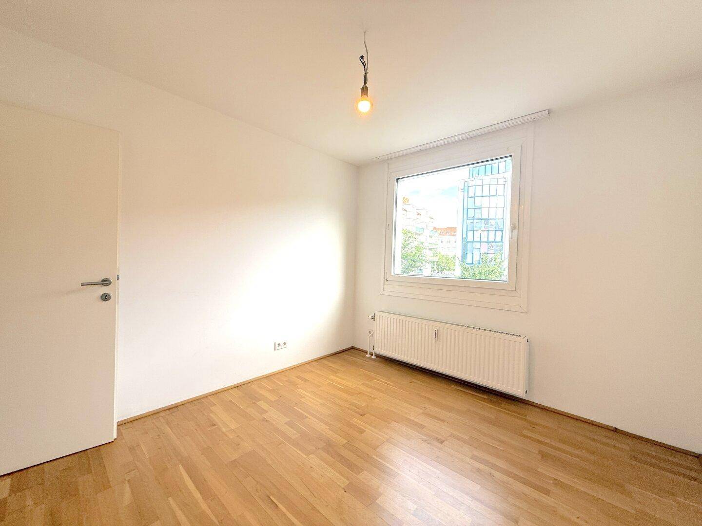 Gemütliches Schlafzimmer mit Parkettboden und einem großen Fenster, das viel Licht hereinlässt.