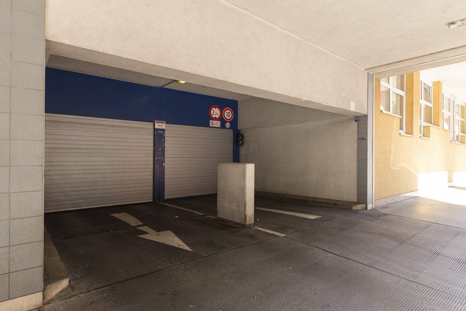Einfahrt zu einer Tiefgarage mit Rolltoren und Hinweisschildern.