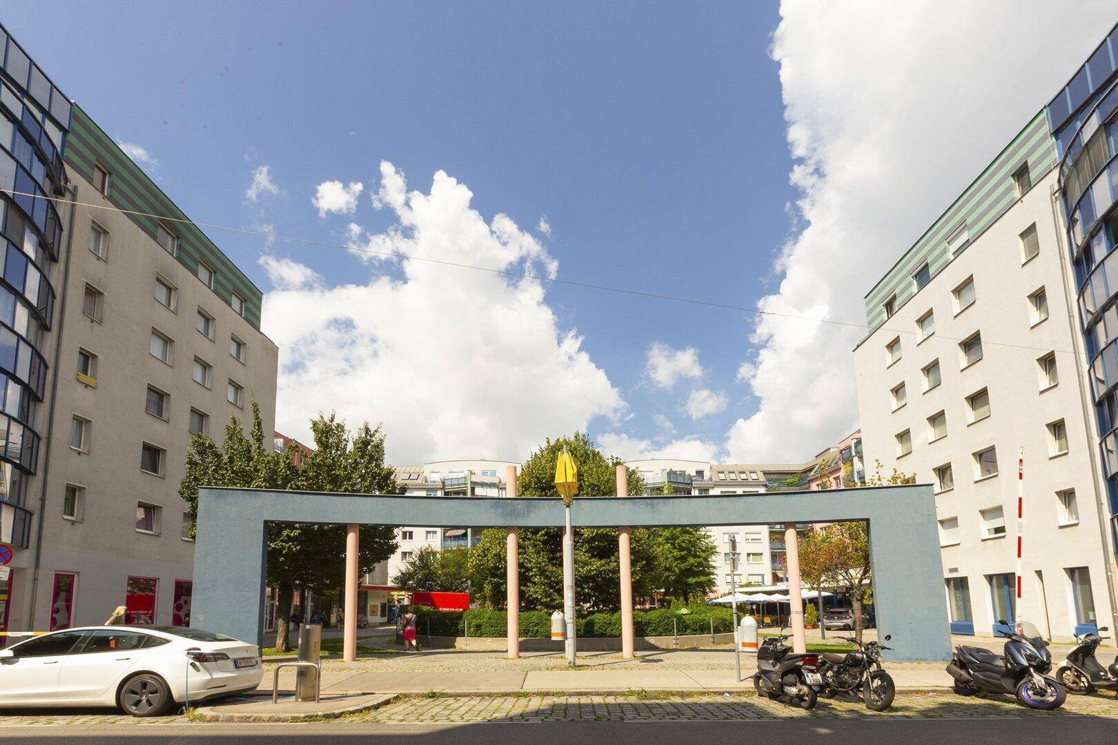 Wohnkomplex mit zentralem Torbogen und begrüntem Innenhof unter blauem Himmel.