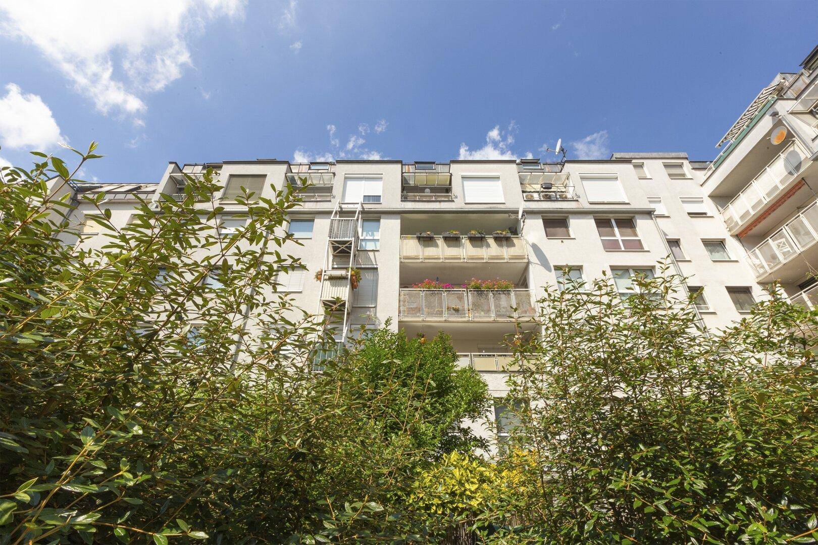 Ansicht einer Wohnhausfassade mit Balkonen, umgeben von üppigem Grün.