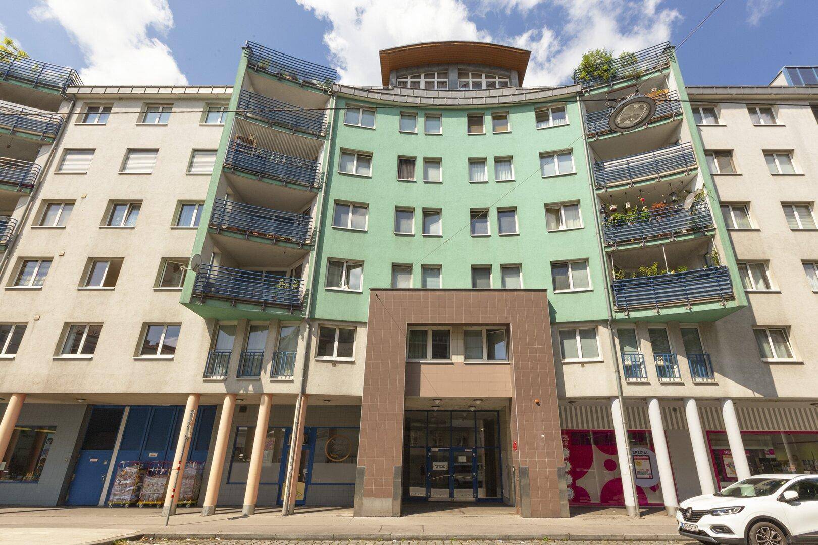 Moderne Wohnhausfassade mit geschwungenen Balkonen und Geschäften im Erdgeschossbereich.