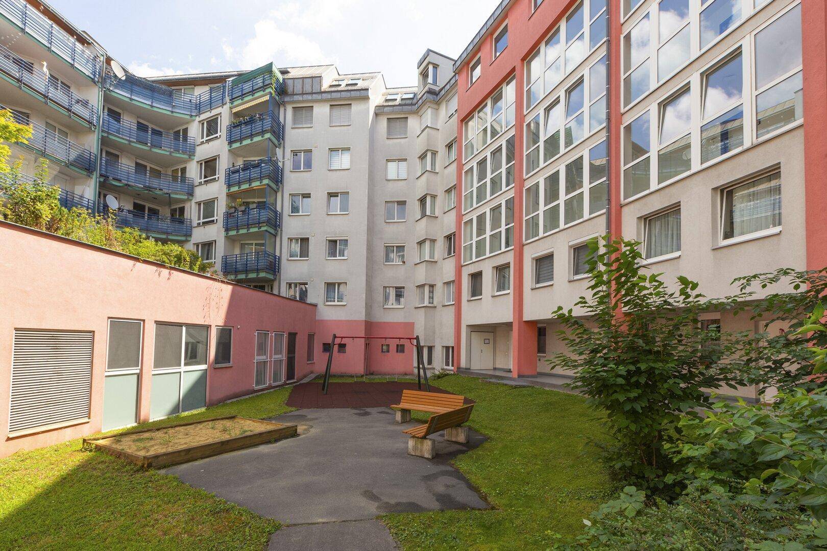 Begrünter Innenhof mit Sandkasten, Schaukel und Sitzbank zwischen den Wohngebäuden.