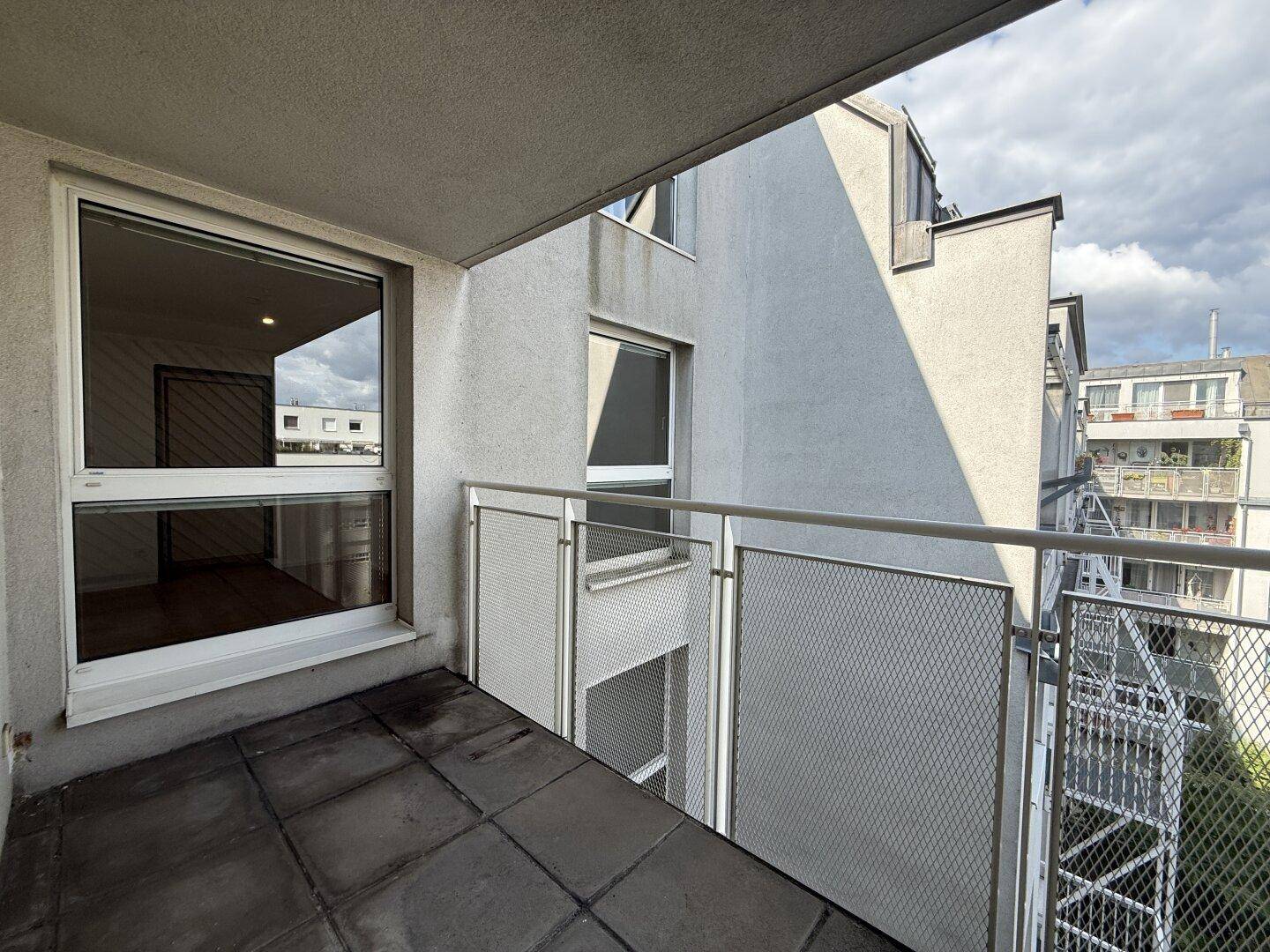 Balkon mit Fliesenboden und Blick auf die umliegenden Gebäude und den Himmel.