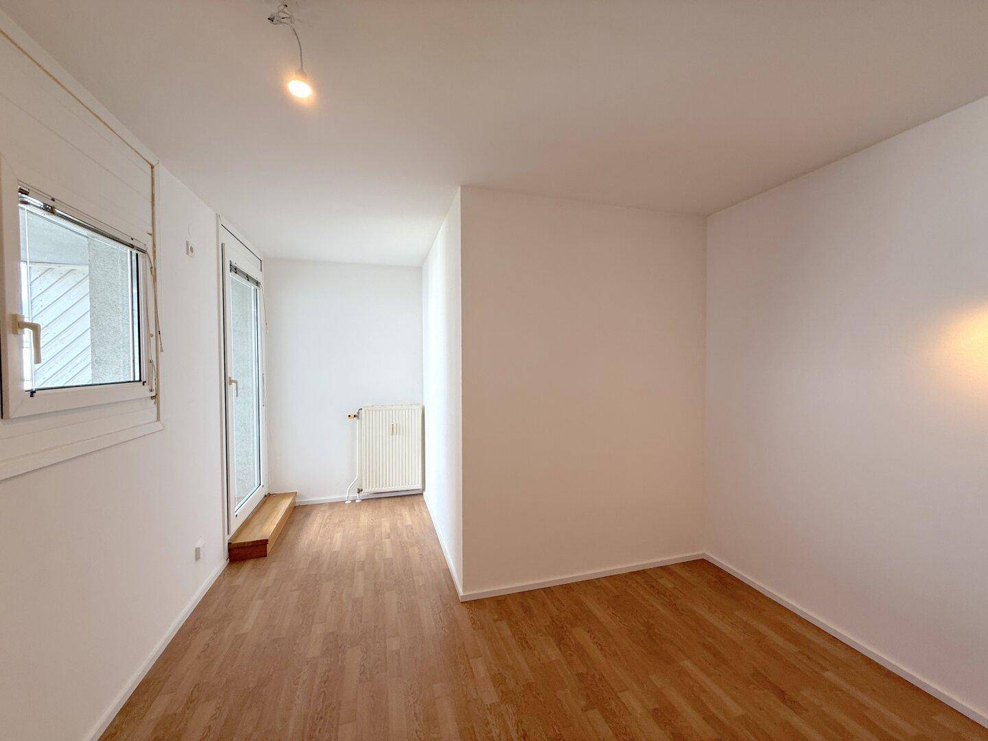 Heller Wohnraum mit Laminatboden und Zugang zum Außenbereich durch eine Fenstertür.