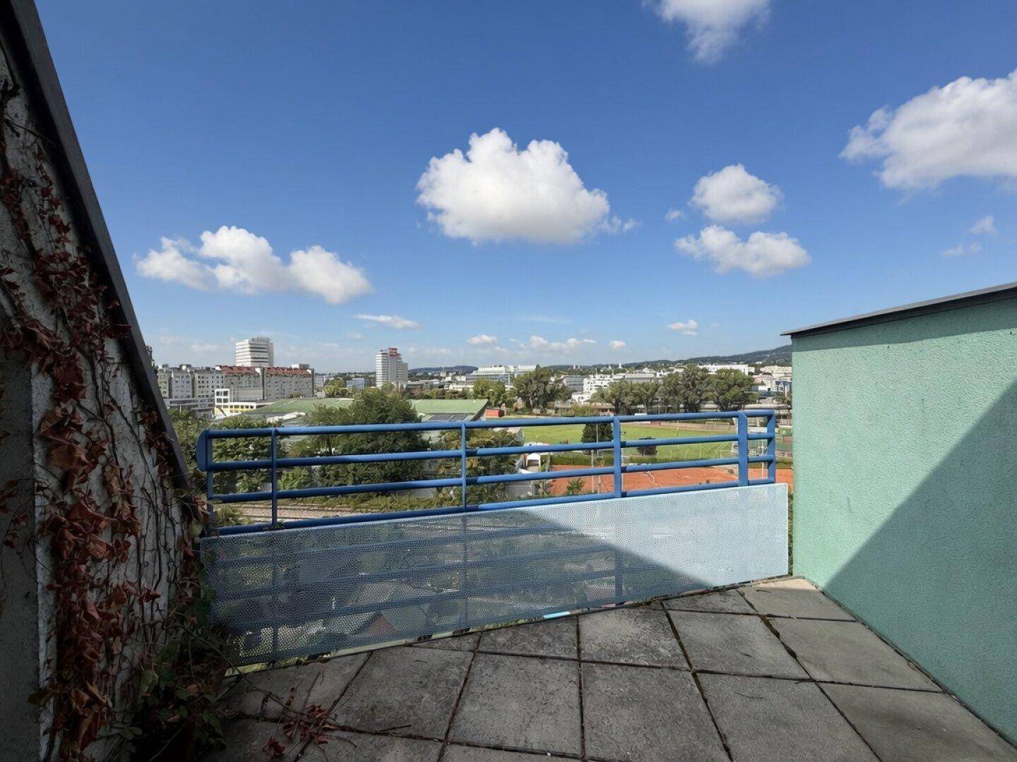 Geräumige Terrasse mit Stadtblick, blauer Brüstung und sonnigem Wetter.