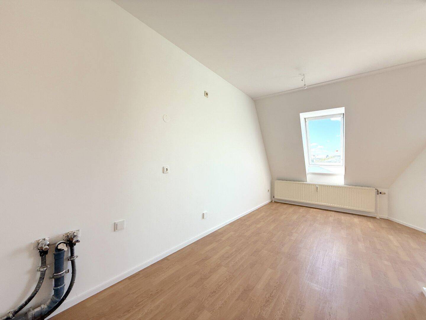 Leeres Zimmer mit Dachschrägen, Laminatboden und einem Dachfenster für natürliches Licht.