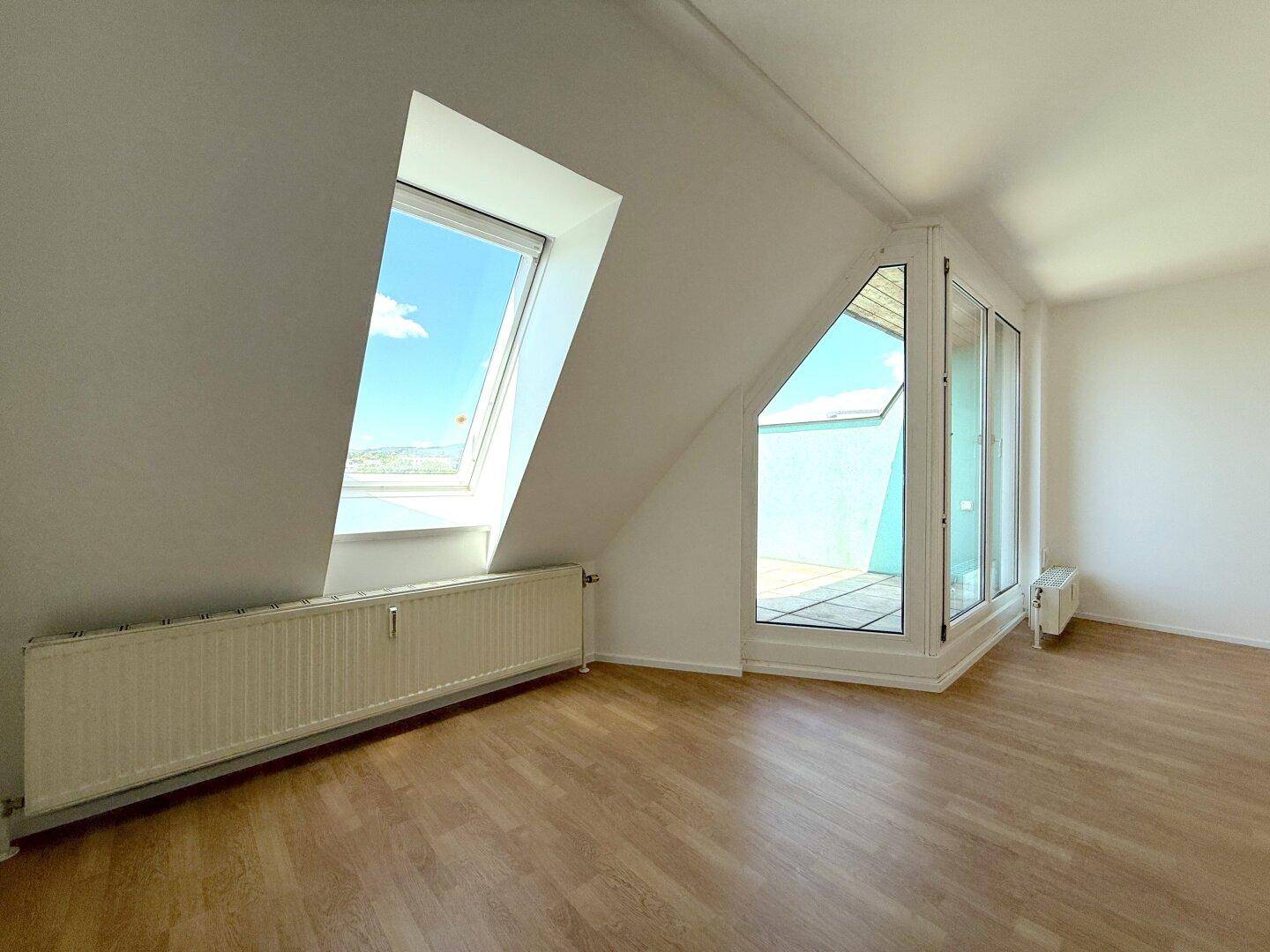 Heller Raum mit Dachschräge, Laminatboden und Zugang zu einem Außenbereich.