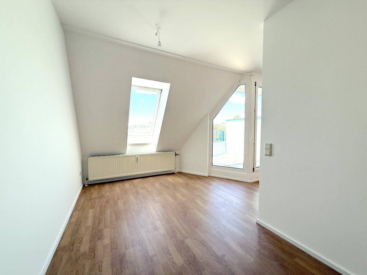 Geräumiges Zimmer mit Laminatboden, Dachschräge und viel Tageslicht durch Fenster und Tür.