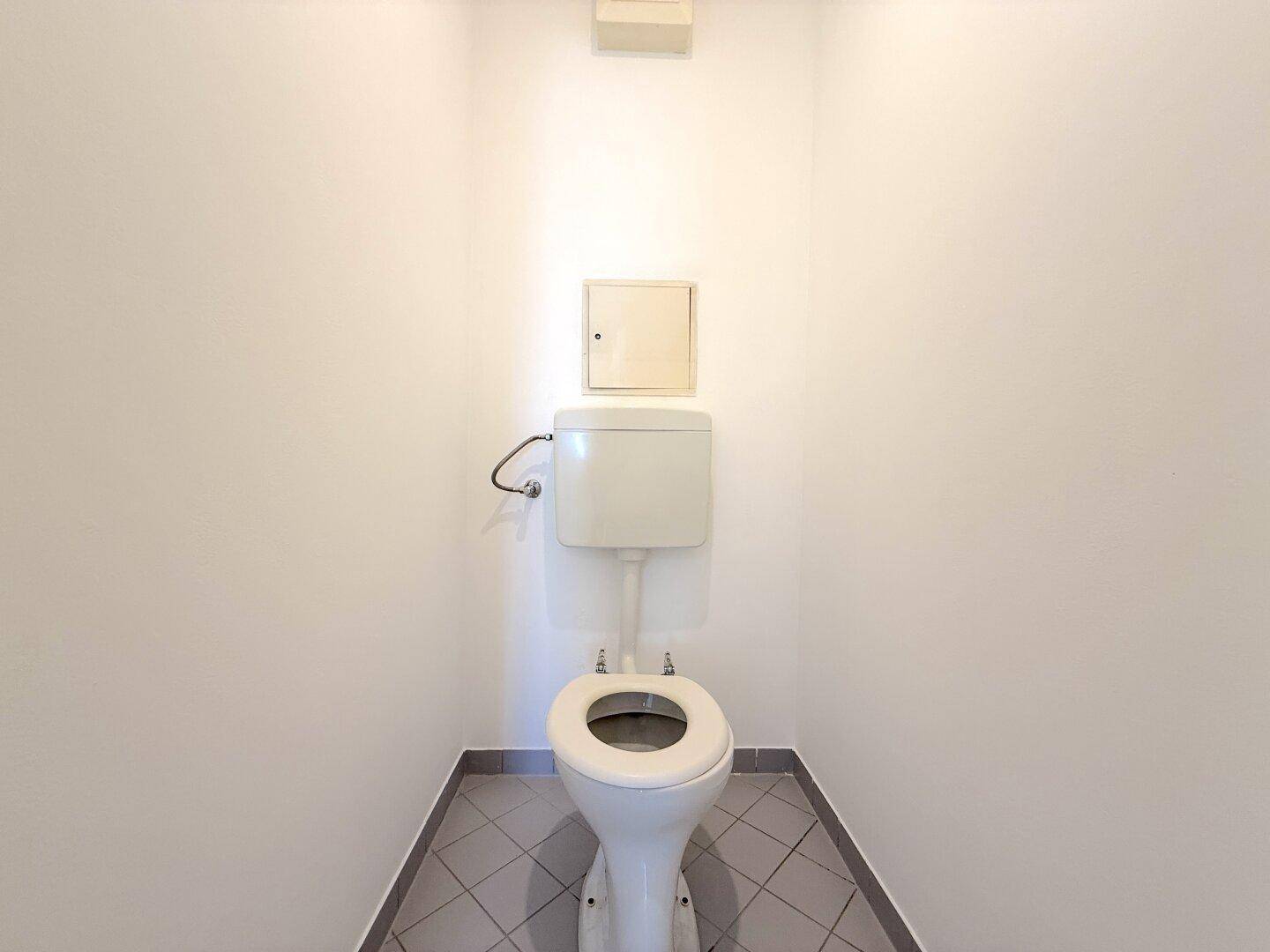 Kleines Gäste-WC mit Toilette und Fliesenboden in schlichtem Design.