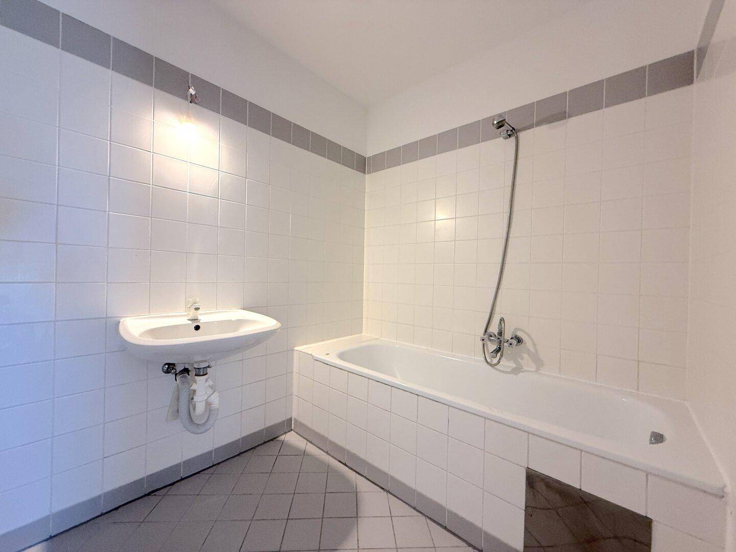 Badezimmer mit weiß gefliesten Wänden, Badewanne und Waschbecken in gutem Zustand.