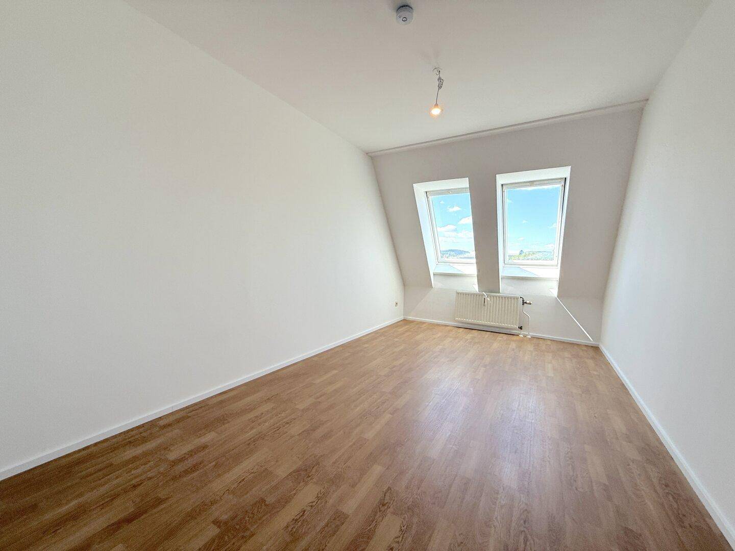 Schlafzimmer mit Laminatboden, Dachschrägen und zwei Dachfenstern für helle Atmosphäre.