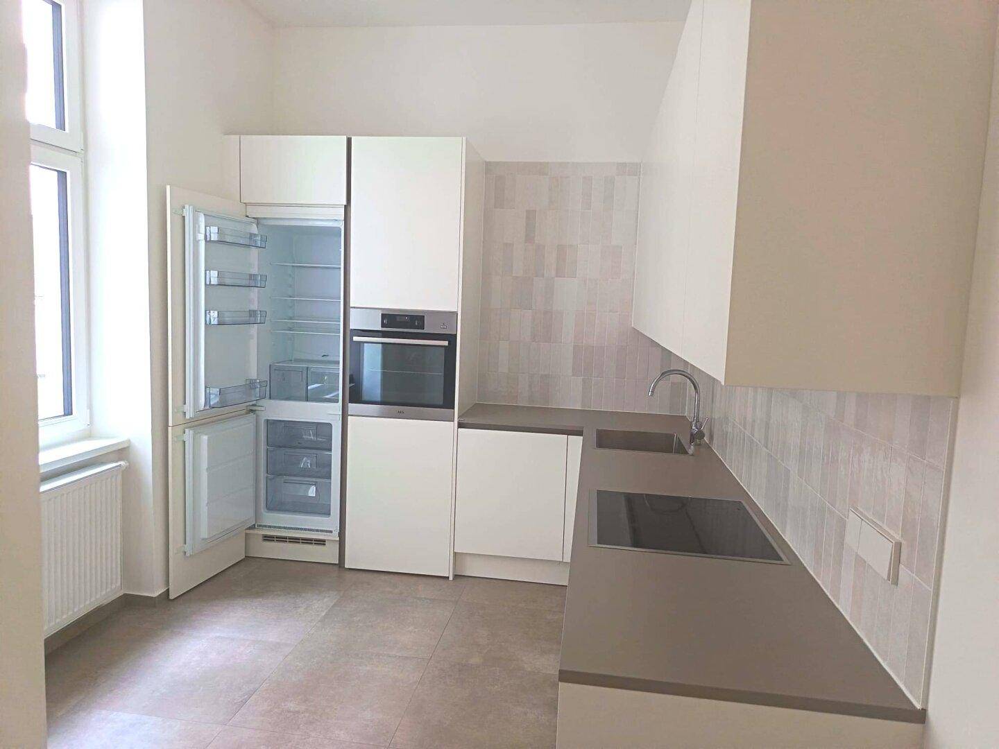 Moderne Einbauküche mit weißen Schränken, integrierten Geräten und Fliesenboden in hellem Design.