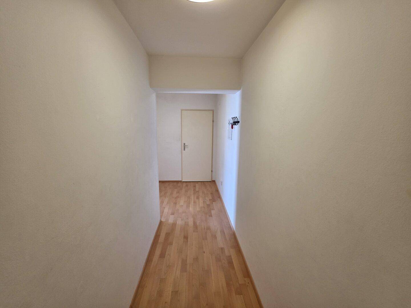 Heller Flur mit Parkettboden und schlichten weißen Wänden, führt zu weiteren Räumen.