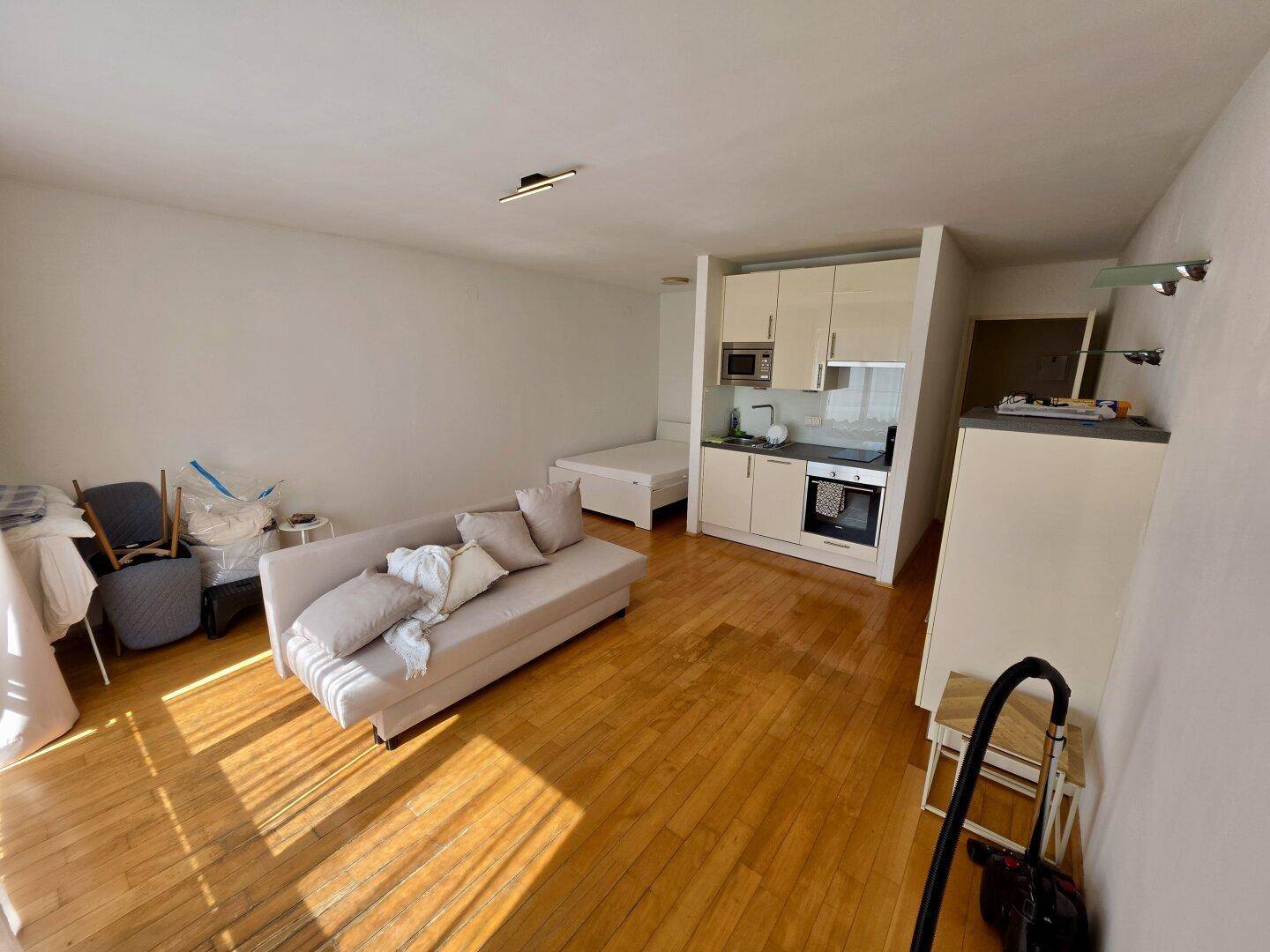 Lichtdurchflutetes Studio-Apartment mit Küchenzeile, Schlafbereich und Parkettboden.
