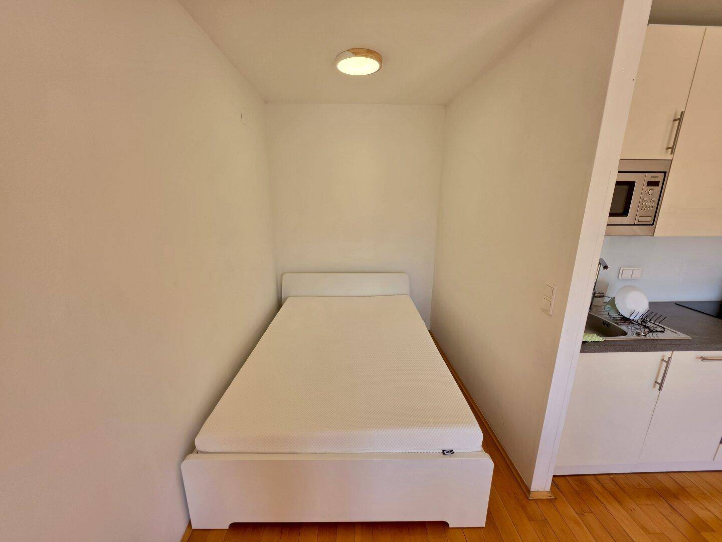 Gemütlicher Schlafbereich mit Einzelbett und heller Wandgestaltung im Studio-Apartment.