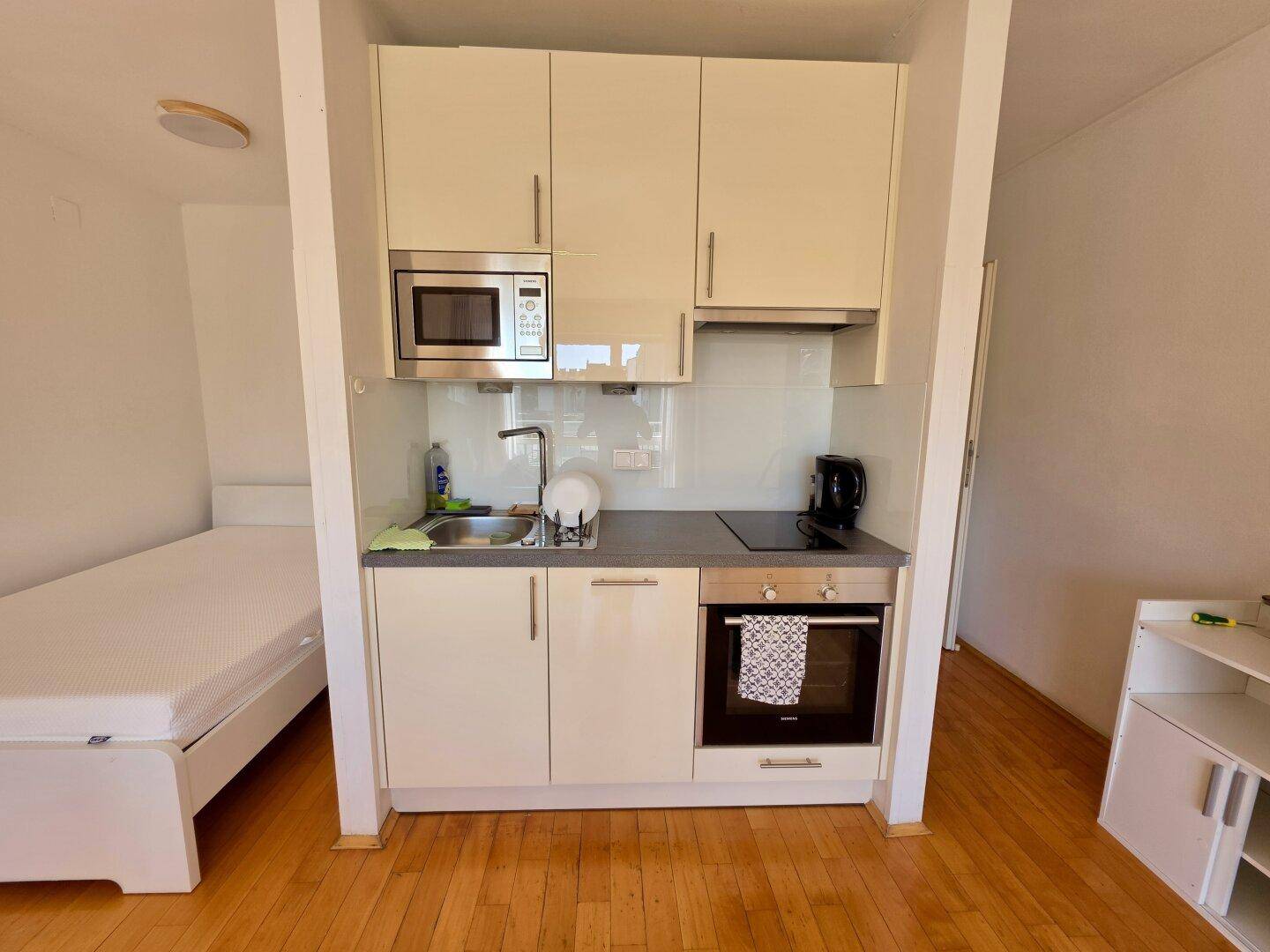 Kompakte Küchenzeile mit Mikrowelle, Kochfeld und Backofen in hellem Design.