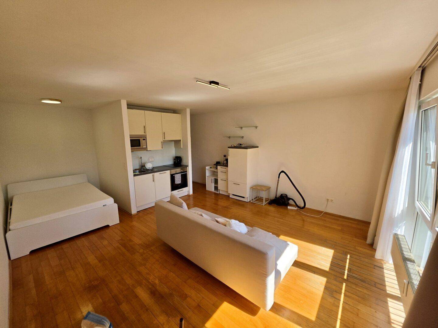 Offenes Studio-Apartment mit Küchenzeile, Schlafbereich und Parkettboden in sonniger Atmosphäre.
