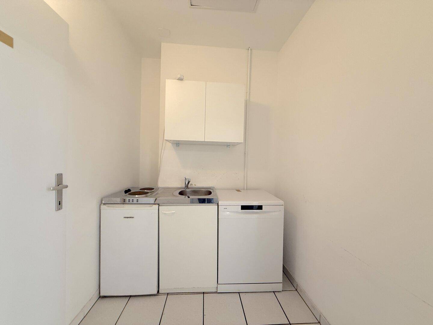 Kleine, funktionale Teeküche mit Spüle, Kochfeld, Kühlschrank und Geschirrspüler in weißem Design.