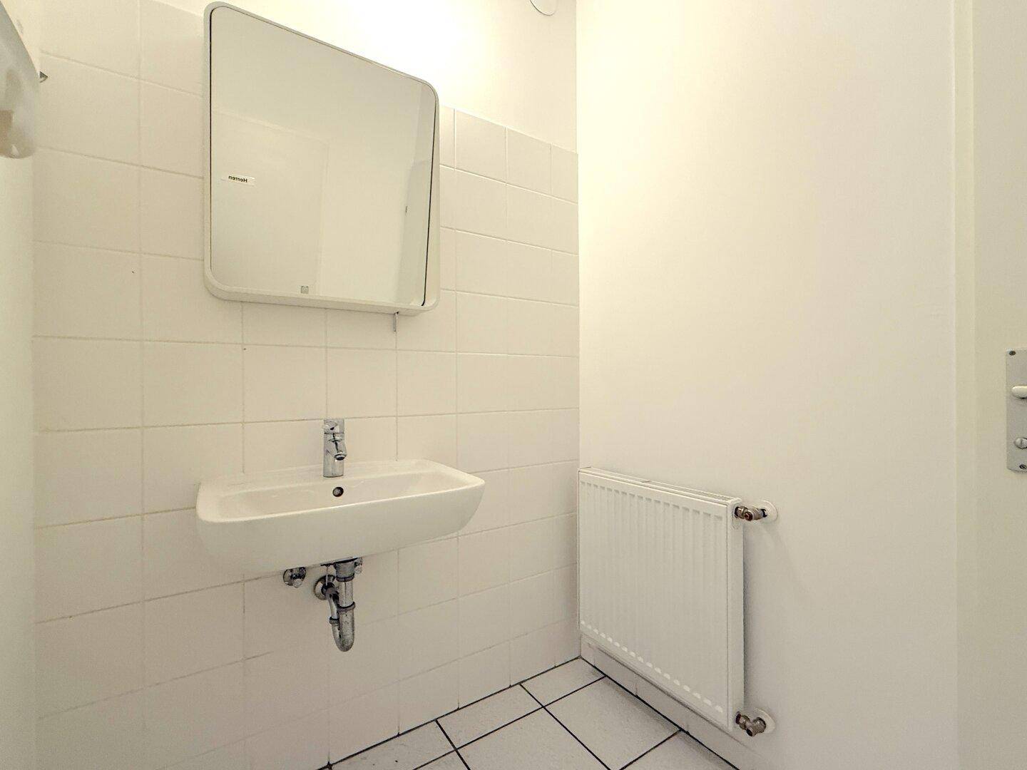 Kleiner Toilettenraum mit Waschbecken, Spiegel und weiß gefliesten Wänden und Boden.