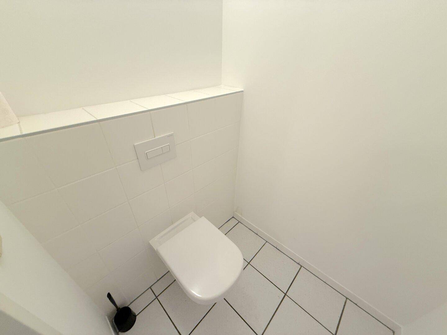 Sauberer Toilettenraum mit wandhängendem WC und weiß gefliesten Wänden und Boden.