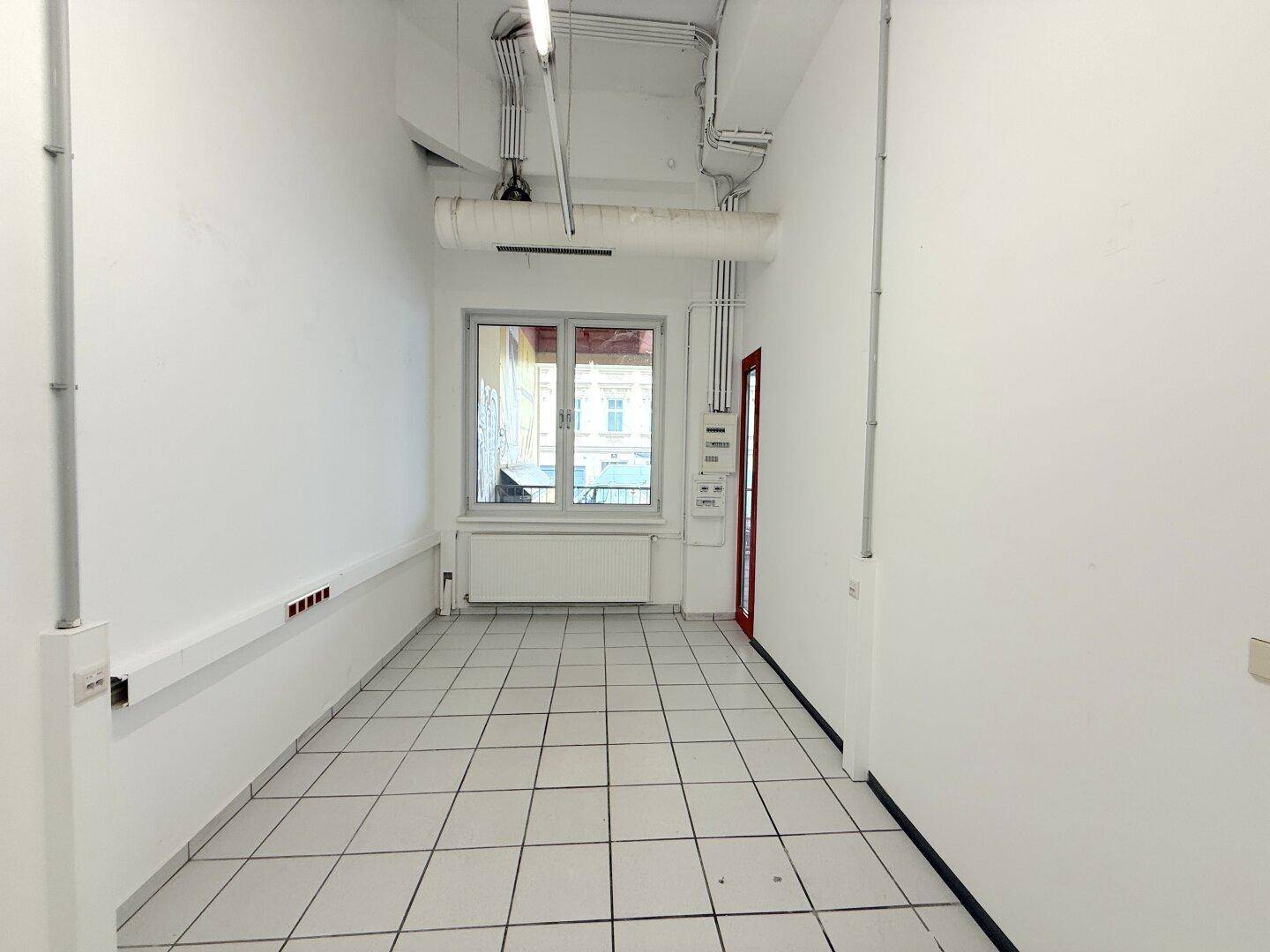 Langer Gewerberaum mit Fenster, Tür und Fliesenboden, ideal für verschiedene Geschäftsnutzungen.