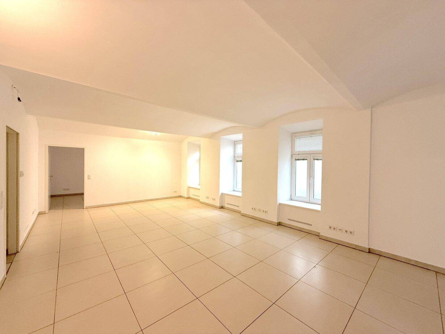 Geräumiger, heller Raum mit Fliesenboden, mehreren Fenstern und gewölbter Decke.
