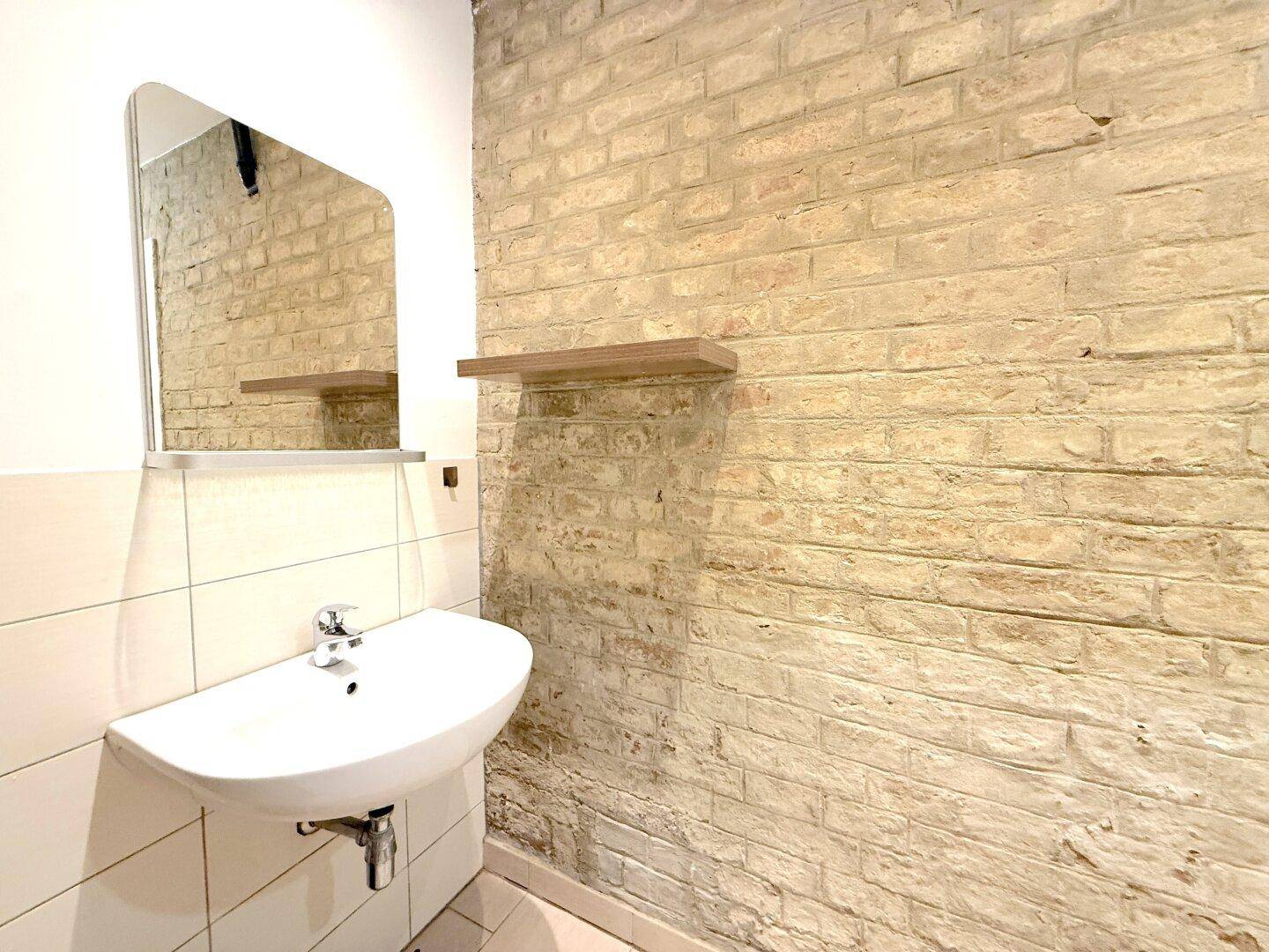Badezimmer mit Waschbecken, Spiegel und einer Wand aus freigelegten Ziegeln.
