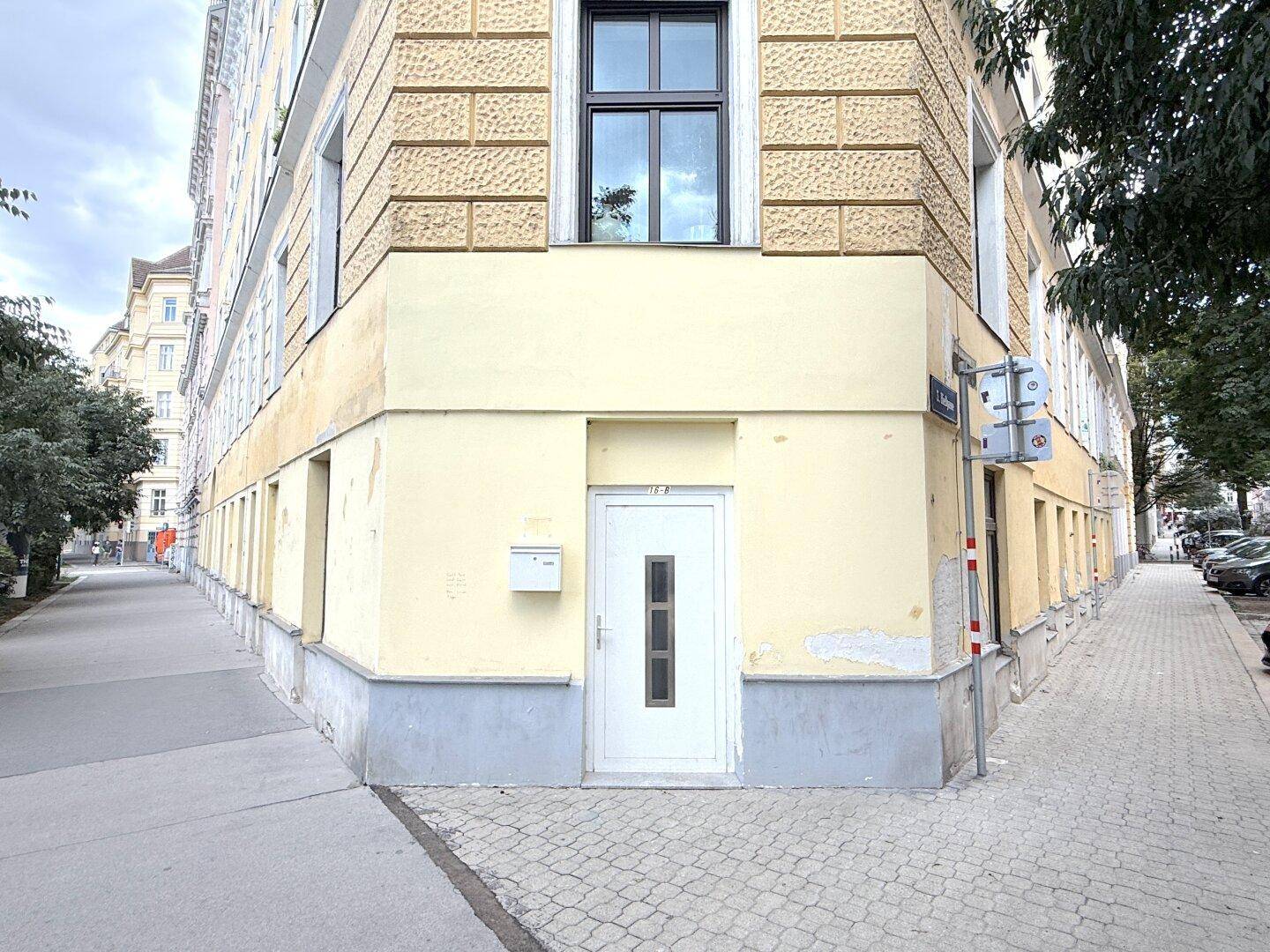 Eckgebäude mit gelber Fassade, Eingangstür und Bürgersteig.