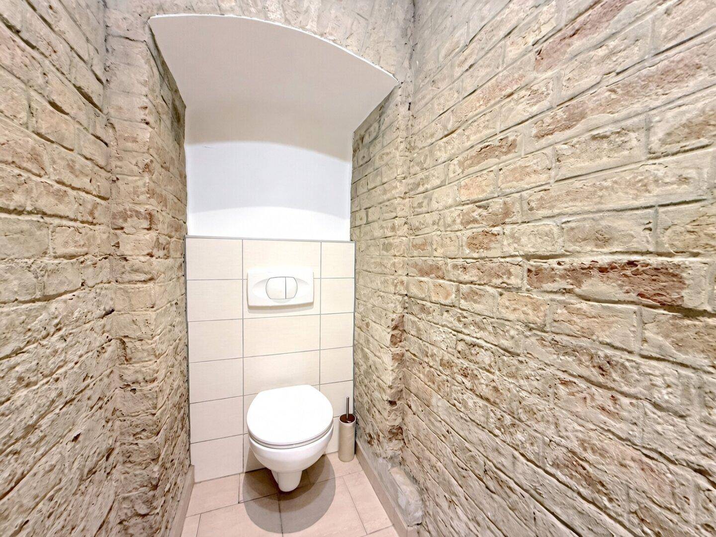 Separate Toilette mit Wand-WC und freigelegten Ziegelwänden.