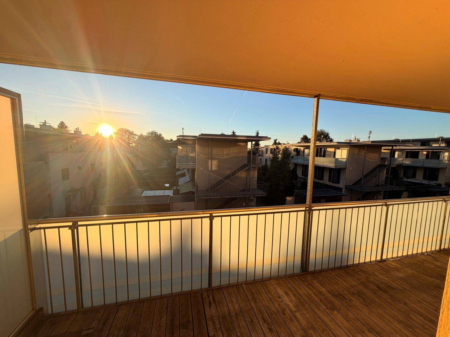 Breiter Balkon mit Holzdielen und weitem Blick über die Wohnanlage im warmen Abendlicht.