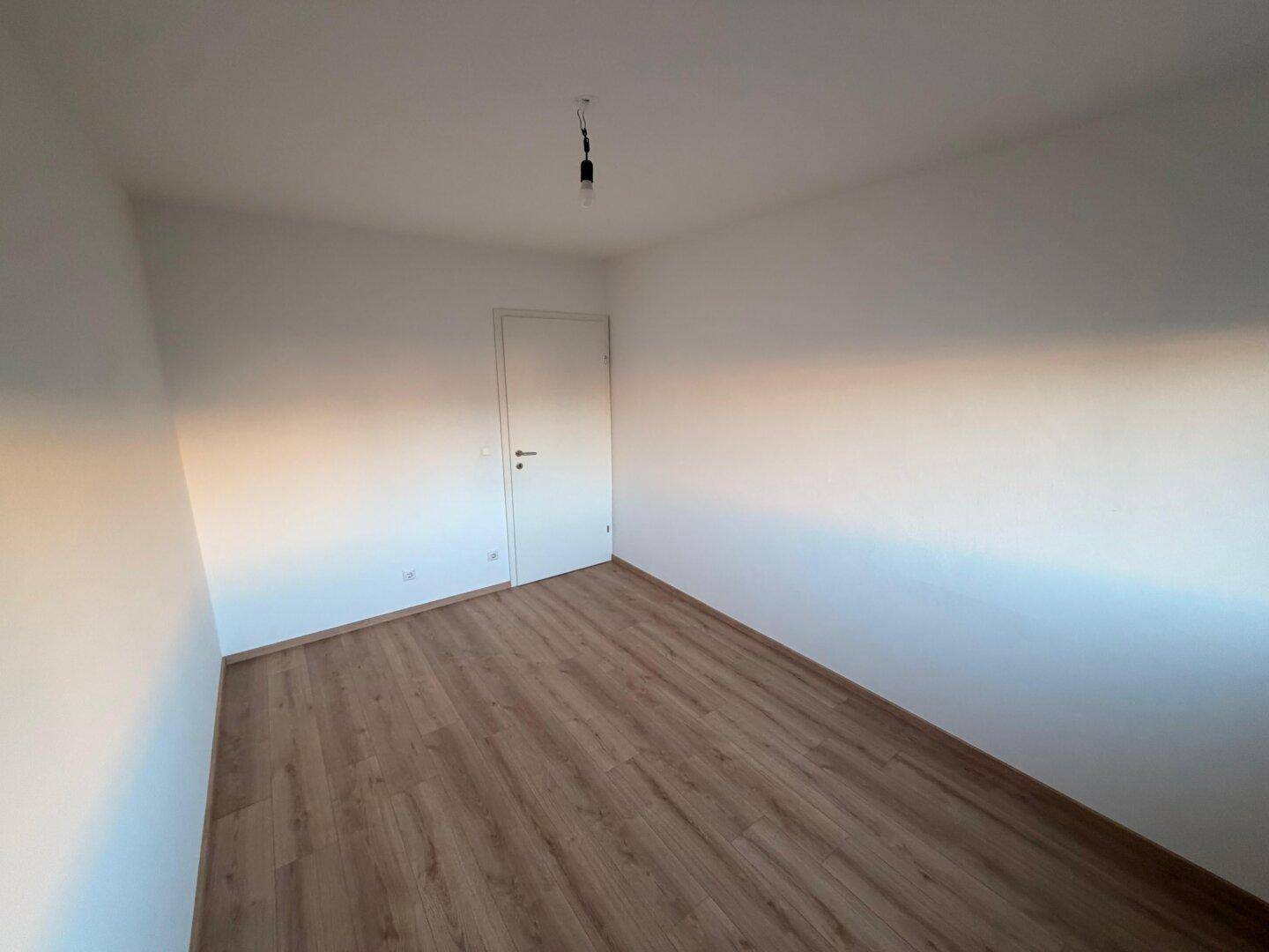 Ruhiges Zimmer mit Laminatboden und weißen Wänden, vielseitig nutzbar als Schlaf- oder Arbeitszimmer.