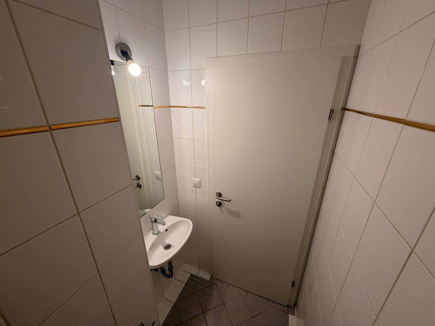 Kleines Gäste-WC mit weißen Fliesen und Waschbecken mit Spiegel, praktisch und funktional.