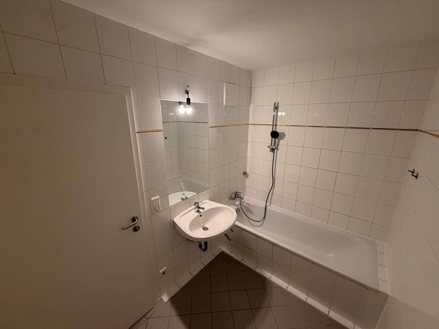 Klassisches Badezimmer mit weißen Fliesen, Badewanne mit Duschfunktion und Waschbecken mit Spiegel.
